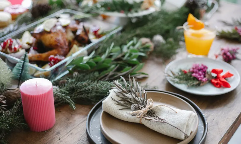 Une volaille rôtie sur un plat au centre d’une table décorée pour Noël, avec des bougies et des branches de sapin.